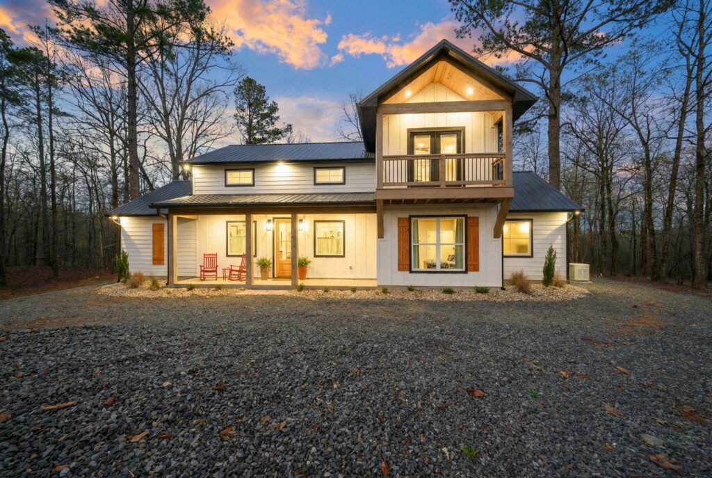 Front exterior of a two-story craftsman-style cabin at twilight with warm interior lighting, dark roof, stone and wood accents, and a gravel driveway surrounded by trees.
