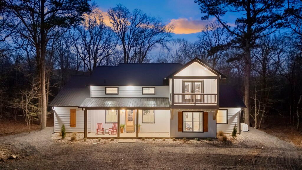 Front view of cabin at dusk with porch lights and balcony surrounded by trees