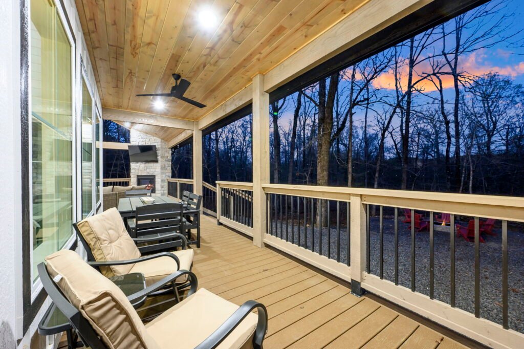 Covered porch with seating area, dining table, and forest view at dusk